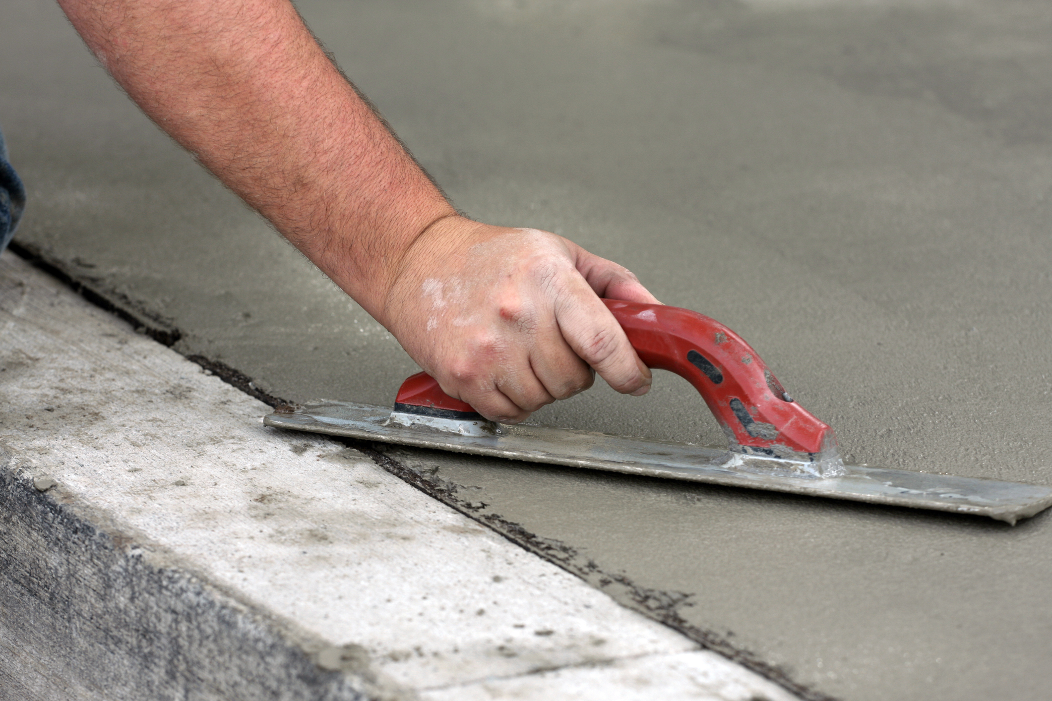 A construction worker trowels concrete on a newly poured sidewalk.